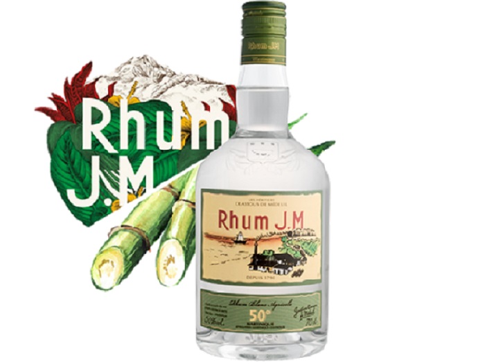 Bouteille de rhum blanc agricole J.M devant des cannes à sucre en Martinique